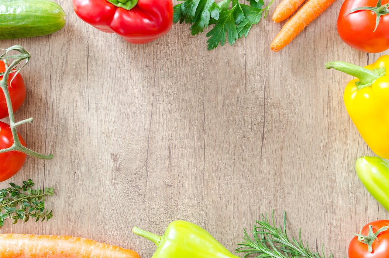 A top view of various fresh organic vegetables arranged on a rustic wooden surface.